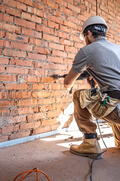 Handyman at a construction site in the process of drilling a wall with a perforator.